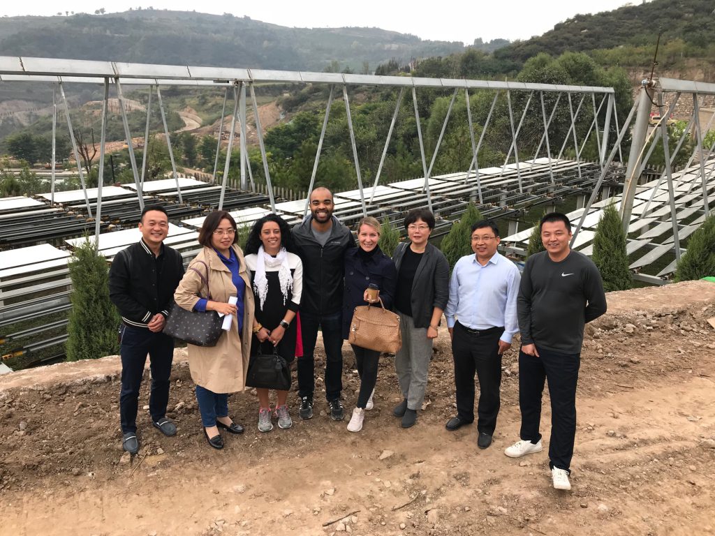 a group of eight poses in front of a solar farm on a Chinese hillside