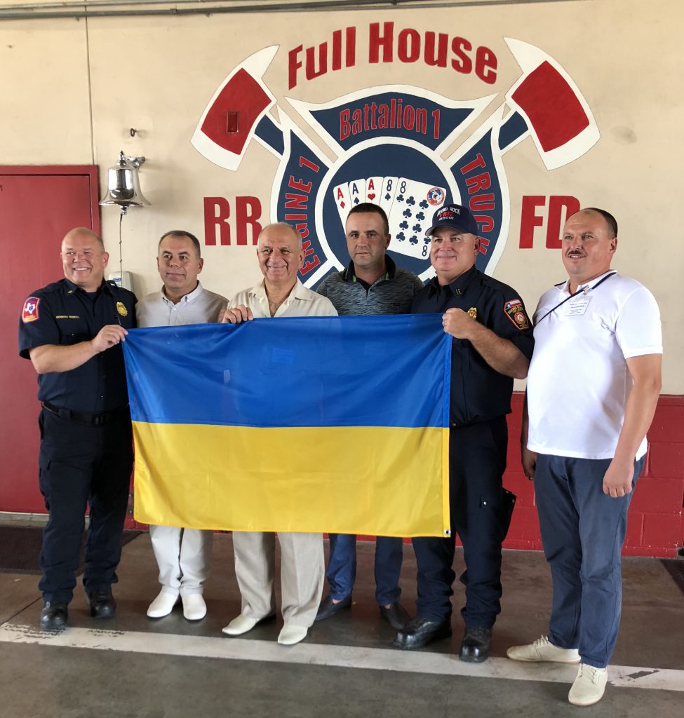 Ukrainian delegates and fireman pose with Ukrainian flag in front of the firehouse 