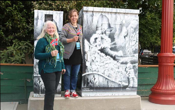 Two people standing in front of utility box wrapped with laminate decal displaying a painting