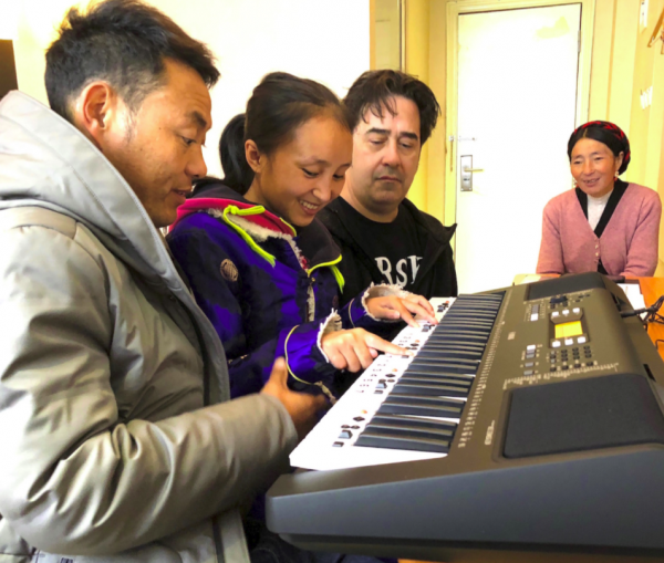 two men play piano with young lady while mother looks on